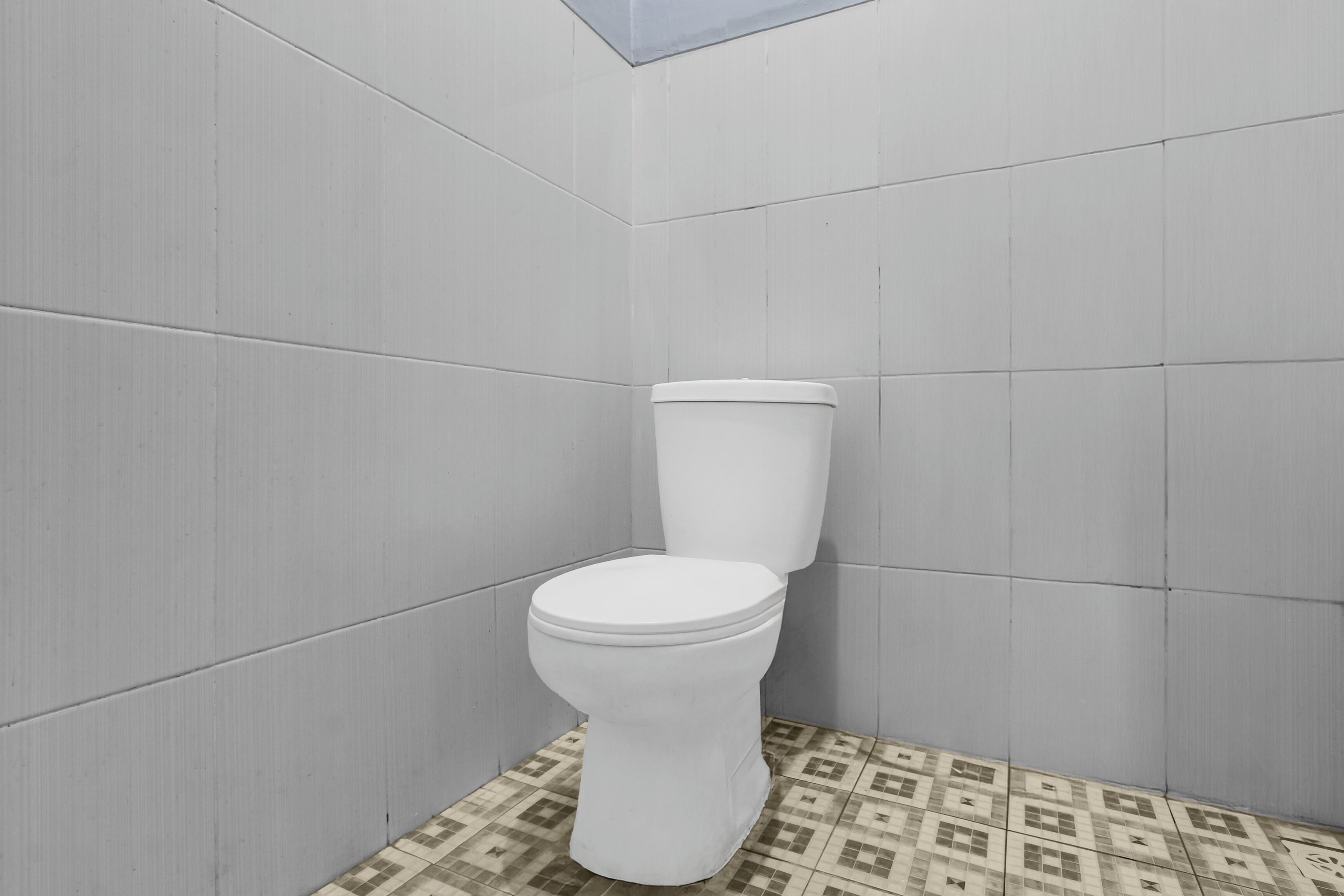 Une salle de bain avec des toilettes, des murs carrelés et un sol à motifs.
