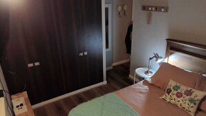 Een slaapkamer met een bed, nachtkastje, lamp en een kledingkast.