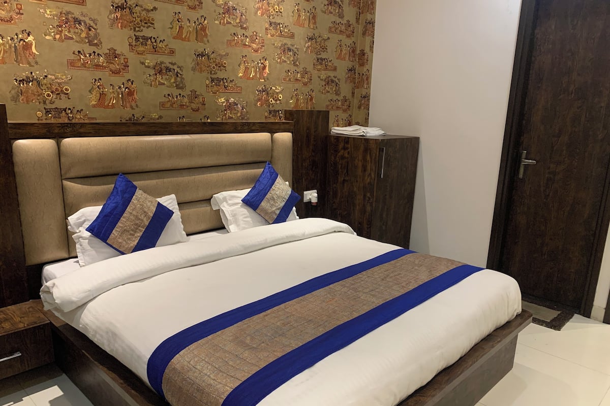 Un lit bien fait, recouvert d’une couvre-lit à rayures bleues et brunes, avec une tête de lit en bois et un mur tapissé d’un papier peint à motifs.