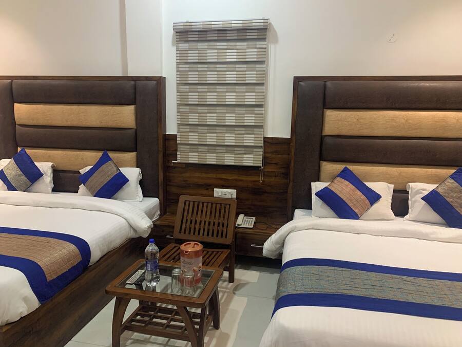 Una habitación de hotel con dos camas individuales, un cabecero de madera, una mesita con superficie de vidrio, un teléfono y una ventana con persianas.
