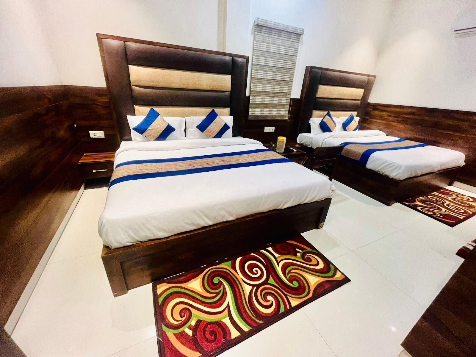 A hotel room with two beds, a window with blinds, a patterned rug, and a wooden floor.
