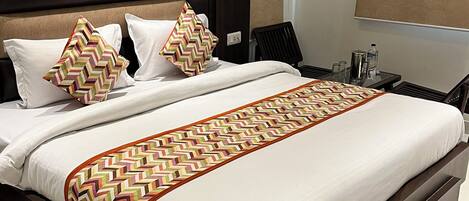 Una habitación de hotel moderna con una cama grande, una mesita de noche, una silla y un ventanal con cortinas.