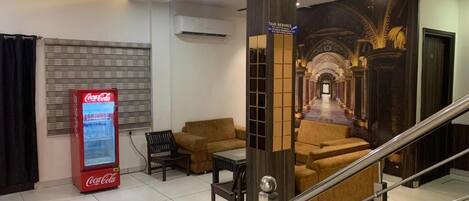 Un hall con un refrigerador de Coca-Cola, sofás, una escalera y un letrero que dice 'Servicio de Taxi'.