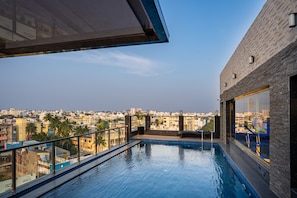 A rooftop pool with a city view, a glass balustrade, and a modern building facade. - Ratan International  (Puducherry)