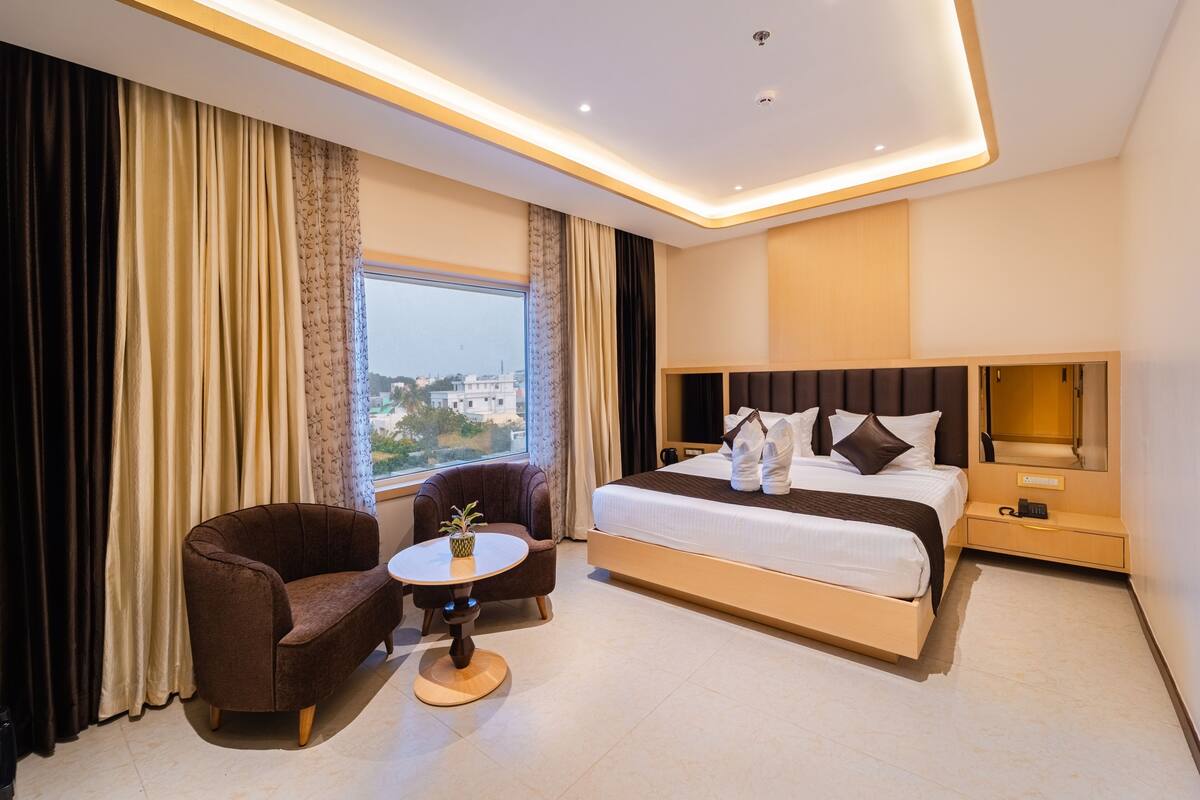 Una habitación de hotel con una cama grande, una silla, una mesita y una ventana con cortinas.