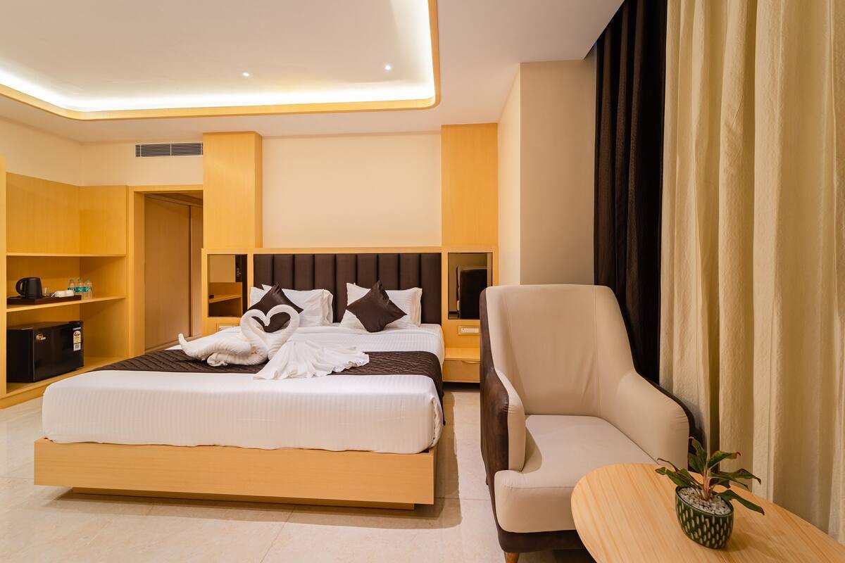 Habitación de hotel con una cama grande, mesitas de noche, una silla, una pequeña mesa con una planta y un armario.