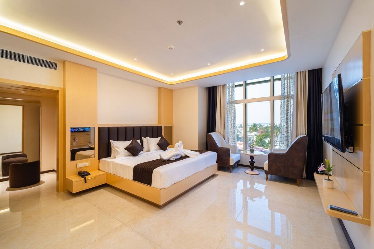 Una habitación de hotel moderna con una cama grande, televisión, zona de estar y vistas al exterior.