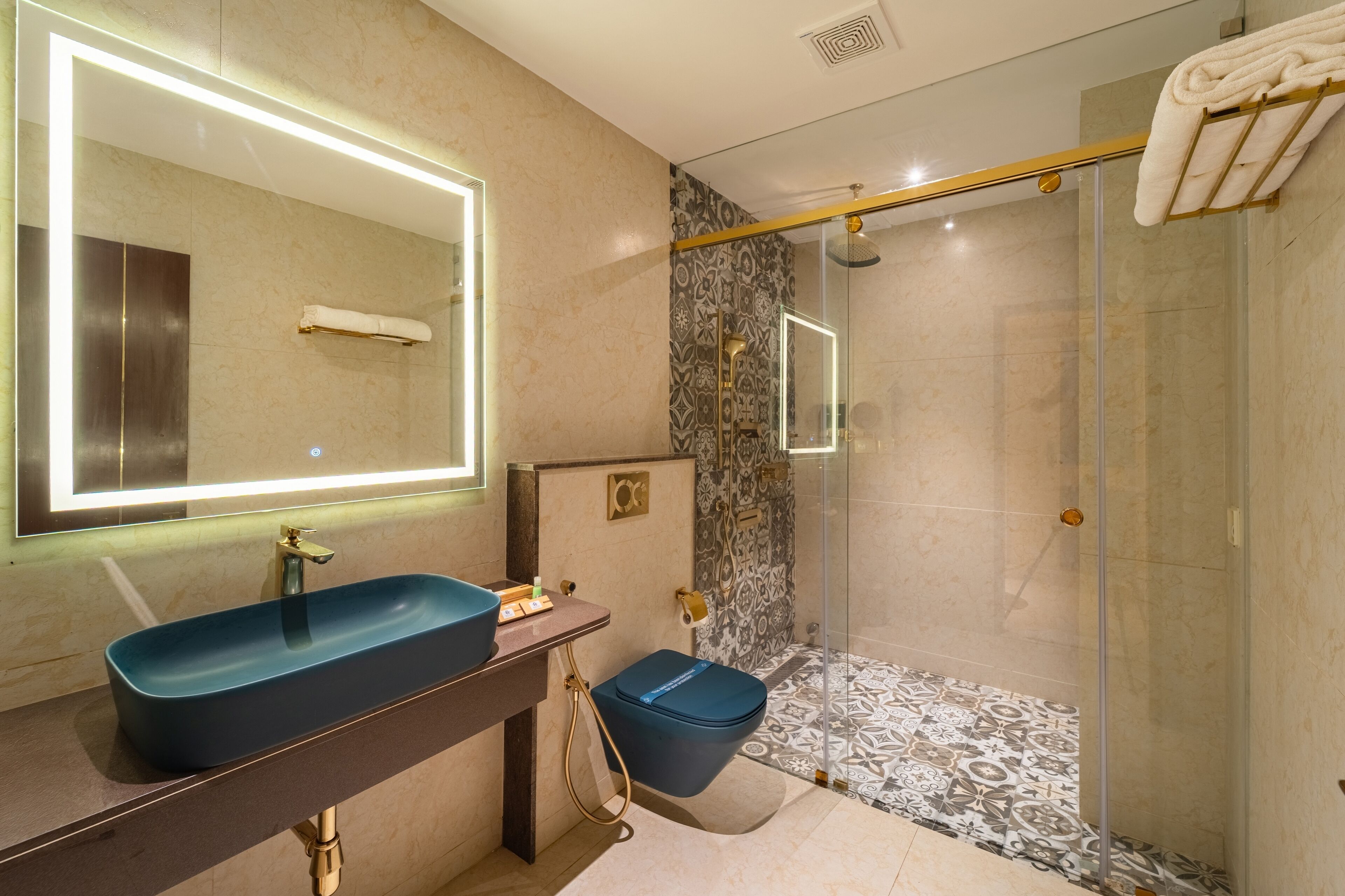 Une salle de bain moderne avec un grand miroir, un lavabo bleu, une douche en verre et des carreaux à motifs.