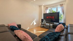 A modern living room with a large flat-screen TV displaying the Netflix logo, a sofa set, and a coffee table. - Spacious 2BR | FREE Parking + 1.5 Bath | Near YUL (Laval)