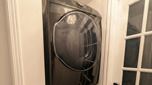 A stacked washer and dryer unit in a hallway with a white door and a window. - Spacious 2BR | FREE Parking + 1.5 Bath | Near YUL (Laval)