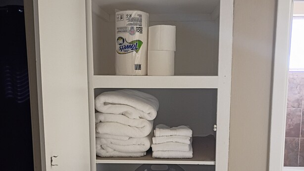 A wardrobe with folded towels, a bottle of lotion, and a trash bin. - Payne Place 1 (Las Cruces)