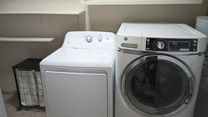 A laundry room with two stacked washers and dryers, a metal laundry cart, and a white wall. - Payne Place 1 (Las Cruces)