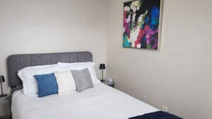 A neatly made bed with white and blue pillows, a grey headboard, and a blue throw blanket. - Payne Place 1 (Las Cruces)