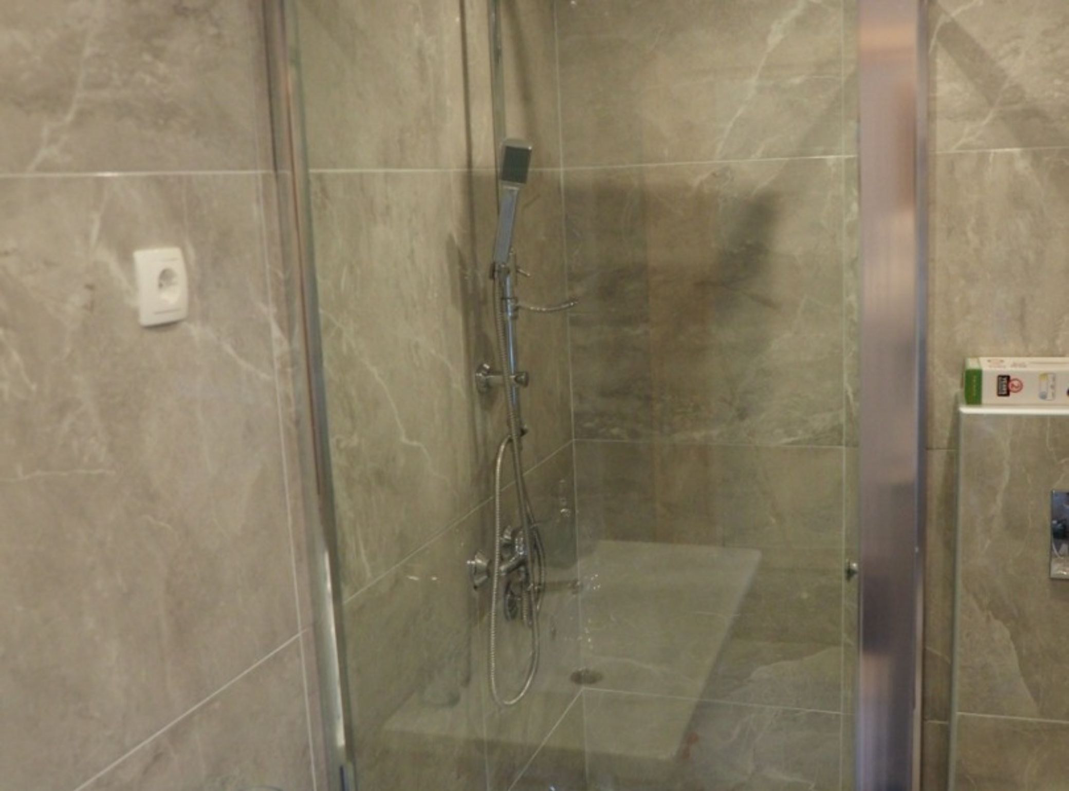 A glass-enclosed shower stall with a handheld showerhead and a wall-mounted faucet.