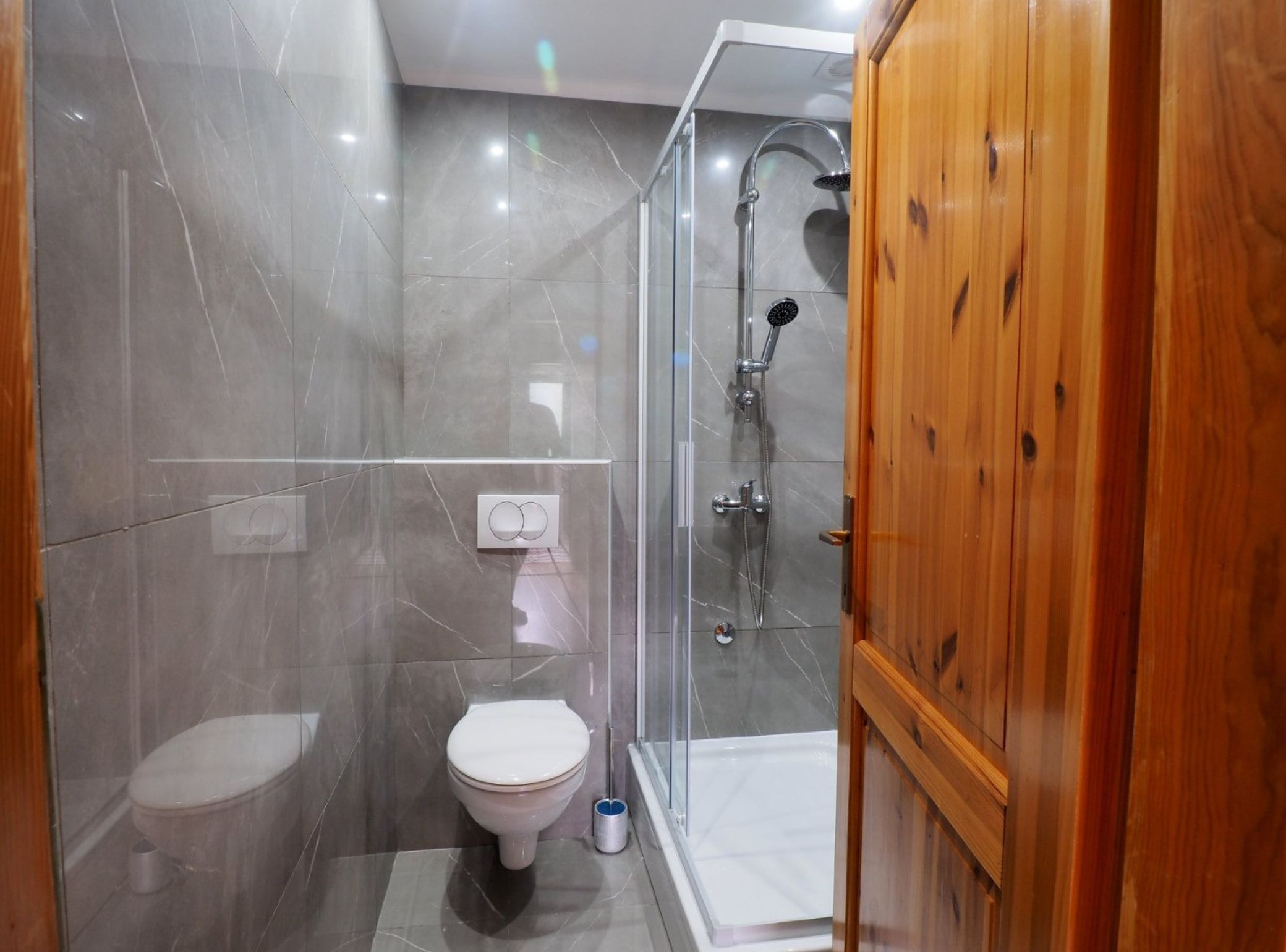 A modern bathroom with a toilet, a shower with a glass enclosure, and wooden cabinets.