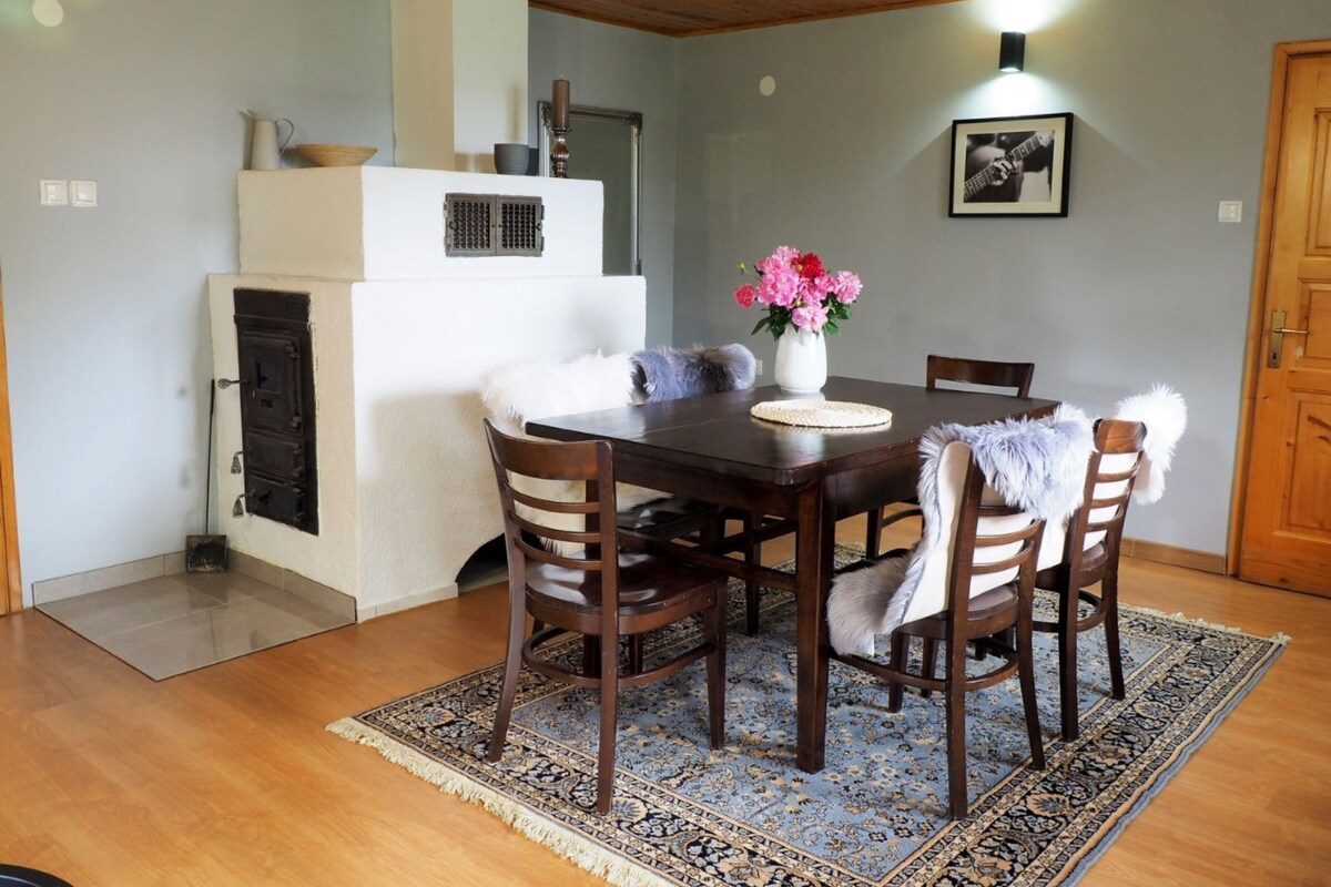 A dining area with a wooden table, four chairs, a rug, a white stove, and a framed picture on the wall.