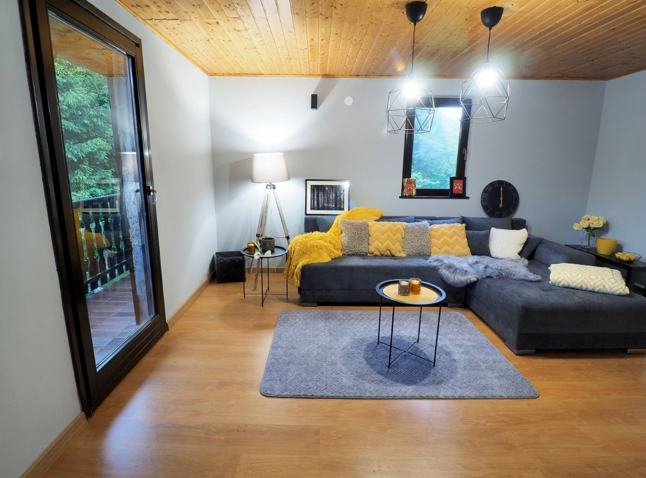 Un salon moderne avec un canapé d’angle gris foncé, un tapis gris et un plafond en bois.