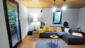 A modern living room with a dark grey sectional sofa, a grey rug, and a wooden ceiling. - Apartments & Rooms Latin (Plaski)