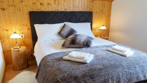 A bed with a dark headboard, white linens, two pillows, and a grey blanket. There are two bedside lamps on wooden stands. - Apartments & Rooms Latin (Plaski)