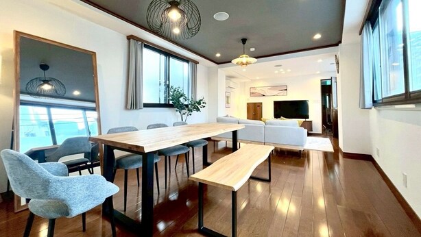 A modern dining area with a wooden table and chairs, a bench, and a large window with curtains. - Yokohama Mega Stay (Yokohama)