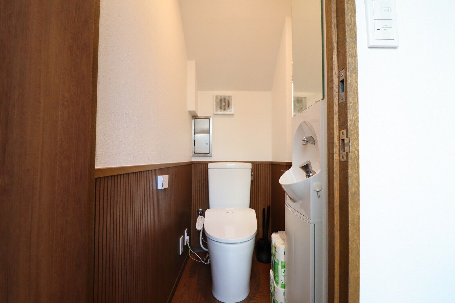 A small, narrow bathroom with a toilet, a sink, and a hand dryer.