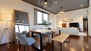 A modern living room with a wooden dining table, gray chairs, a sofa, and a TV. - Yokohama Mega Stay (Yokohama)