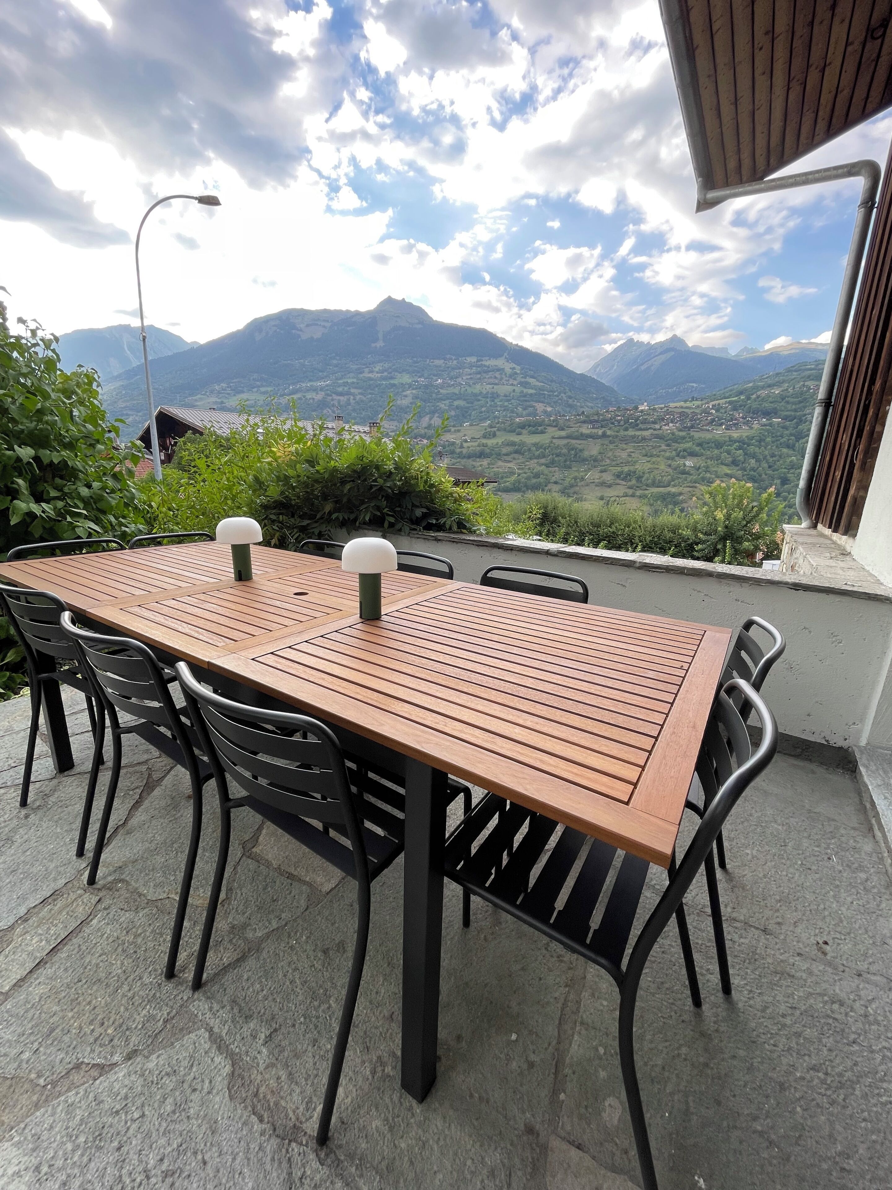 An outdoor dining area with a table and chairs, a lamp, and a view of mountains.