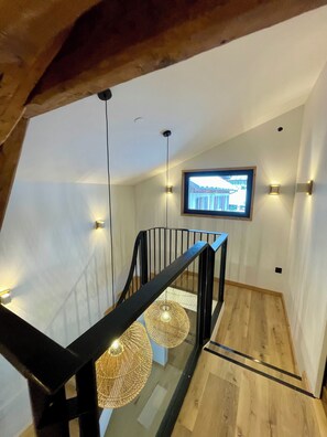 A modern staircase with a glass railing, pendant lighting, and a television mounted on the wall. - MAURICETTE Chalet—Fully Renovated in La Plagne, Ideal for Families (6 adults/4 children) (La Plagne Tarentaise)