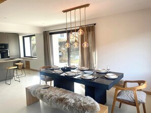 Un espace repas moderne avec une table bleu foncé dressée pour quatre personnes, un banc recouvert de fourrure et une cuisine en arrière-plan.