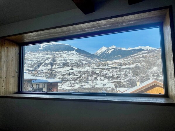Une vue par la fenêtre sur un paysage montagneux enneigé, avec un village en contrebas.