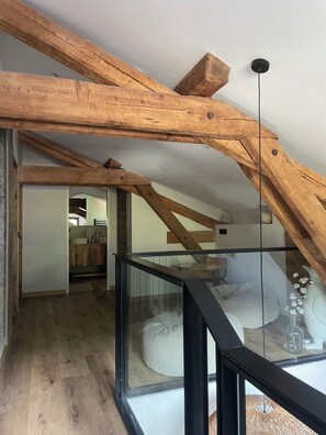 A modern loft with exposed wooden beams, a glass railing, and a view of a kitchen and living area. - MAURICETTE Chalet—Completely renovated in La Plagne, ideal for families (6 adults/4 children) (La Plagne Tarentaise)