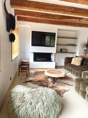 A modern living room with a fireplace, wooden beams, a mounted TV, and a plush fur rug. - MAURICETTE Chalet—Fully Renovated in La Plagne, Ideal for Families (6 adults/4 children) (La Plagne Tarentaise)