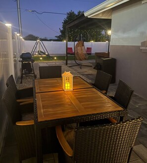 Eine Terrasse im Freien mit einem Holztisch, Korbstühlen, einem Hängesessel und einer Laterne.