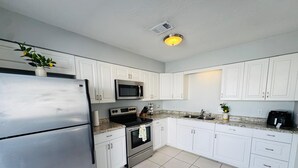 Una cucina moderna con mobili bianchi, elettrodomestici in acciaio inossidabile e pavimento piastrellato.