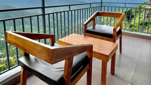 A balcony with two wooden tables and chairs, overlooking a mountainous landscape.