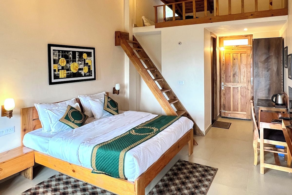 A bedroom with a wooden bed, a staircase, a wooden desk, and a view of the outside.