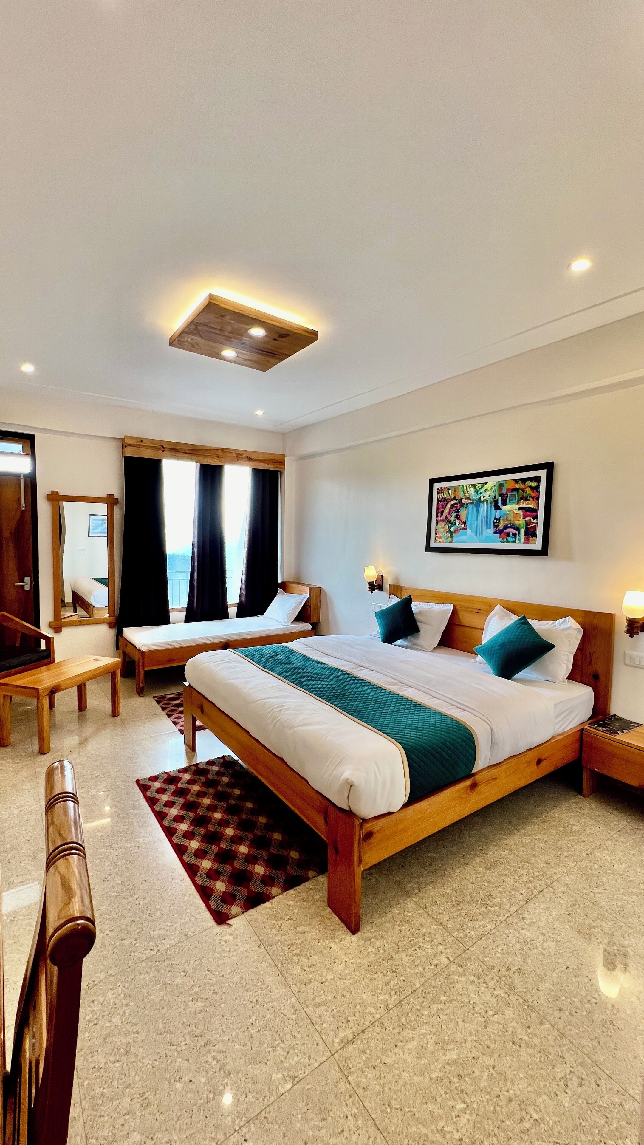 Habitación de hotel con dos camas, un escritorio, una silla, un espejo, una ventana con cortinas y un cuadro en la pared.