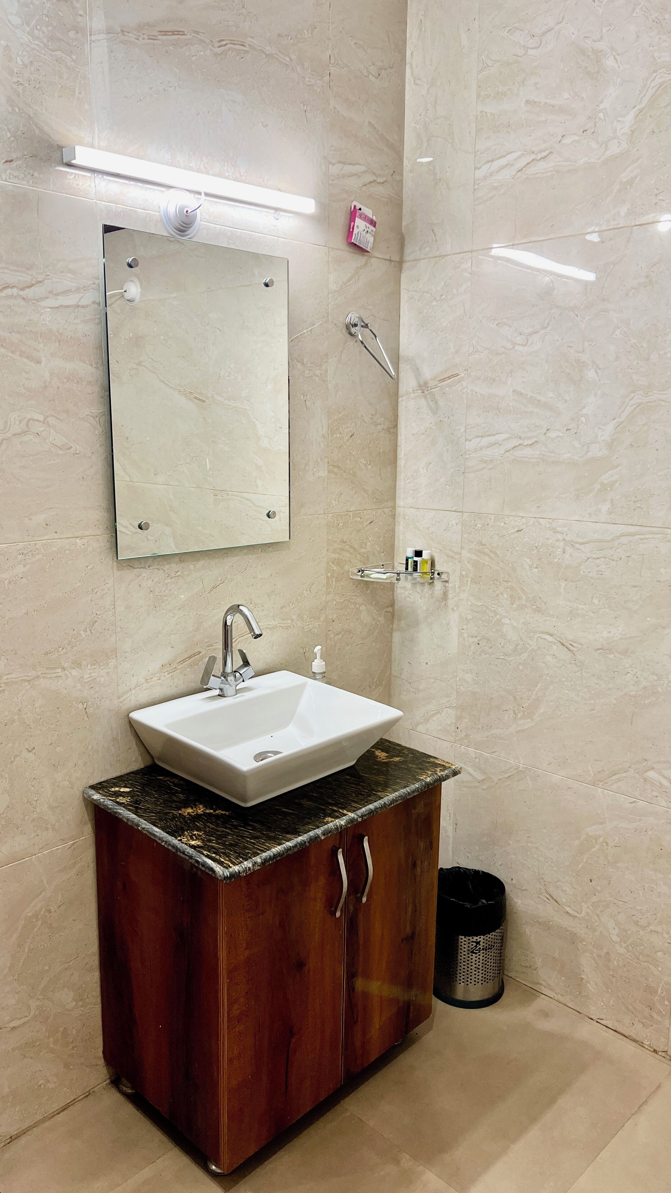 A bathroom with a white sink, wooden cabinet, marble walls, and a mirror.