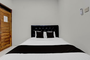 Een enkel bed met een zwart hoofdeinde, wit beddengoed en een houten garderobe.