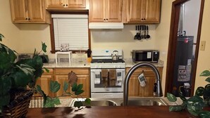A kitchen with wooden cabinets, a stove, a microwave, a sink, and a water heater. - Spacious 4-bedroom house in welcoming Mobile with AC (Mobile)