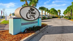 A sign for Palm Cove Private Residential Community with a clear road and palm trees in the background. - Beach Access ! Pool ! Walk 2 Shipwreck Waterpark (Panama City Beach)