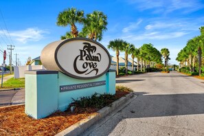 Cartel de la comunidad residencial privada Palm Cove, con una carretera despejada y palmeras al fondo.
