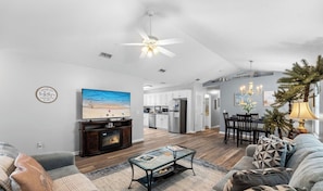 A modern living room with a fireplace, a television, and a dining area with a chandelier. - Beach Access ! Pool ! Walk 2 Shipwreck Waterpark (Panama City Beach)