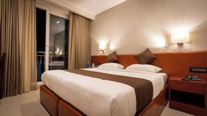 A hotel room with a large bed, a nightstand, a lamp, and a view of the outside through a sliding door. - AS Suites (Kanayannur)