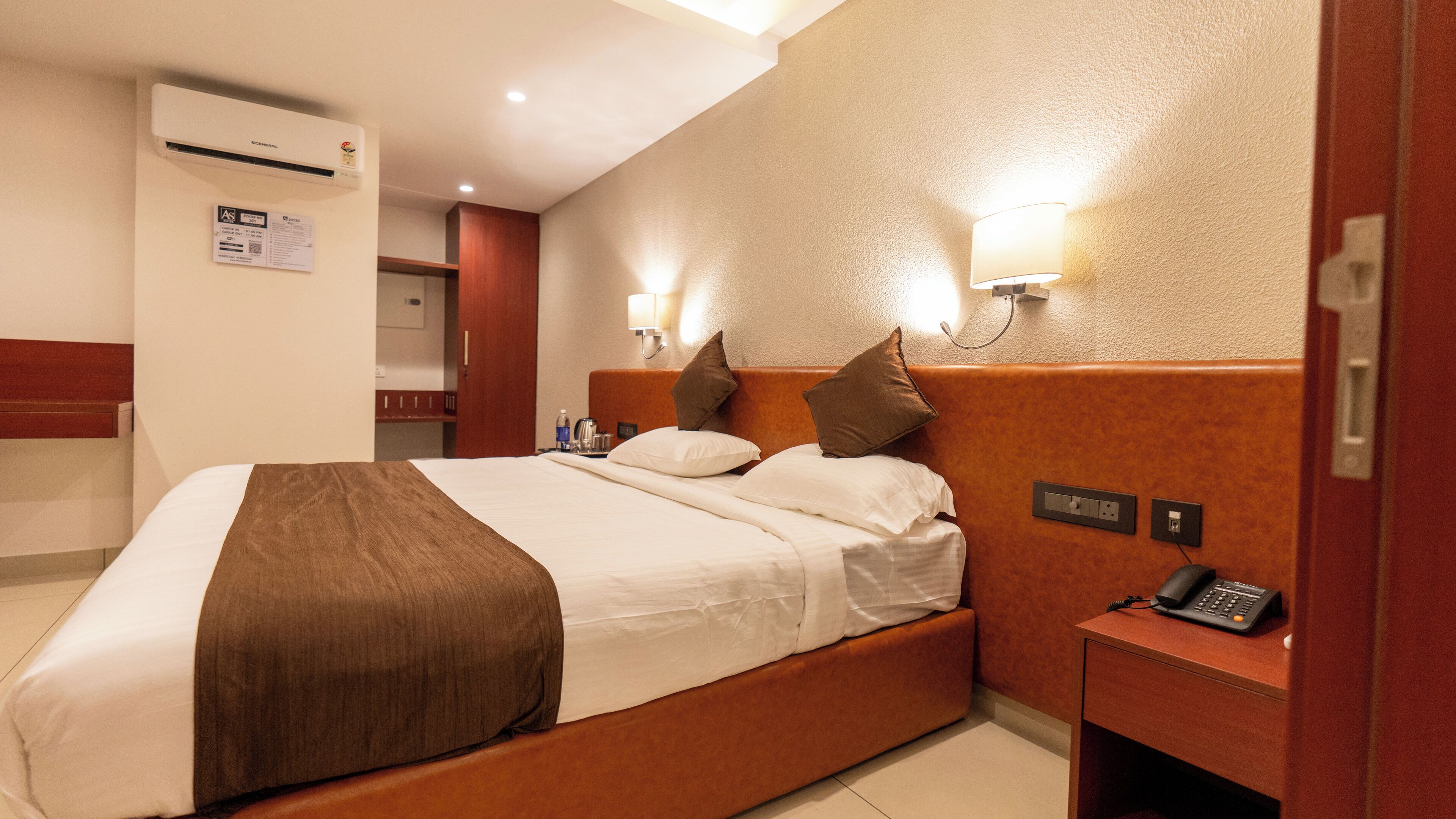 A hotel room with a large bed, a bedside table with a phone, and a wall-mounted light fixture.