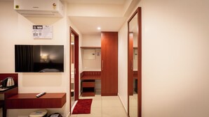 A hotel room with a television, a desk with a remote control, a red rug, and a kitchenette area. - AS Suites (Kanayannur)