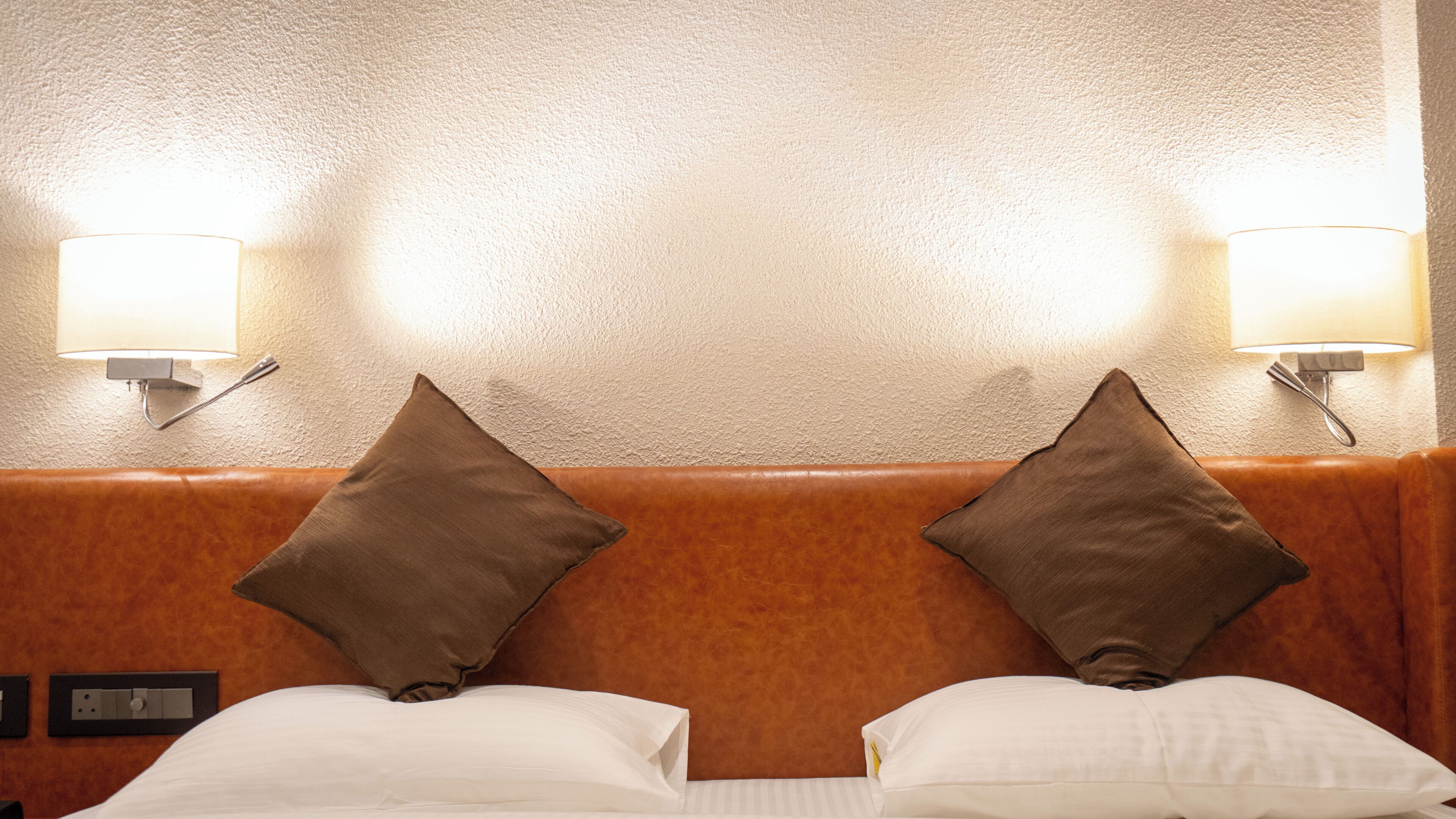Habitación de hotel con cabecera, dos almohadas, una cama y dos lámparas fijadas a la pared.