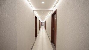 A long, narrow hotel corridor with doors on both sides, recessed lighting, and a tiled floor. - AS Suites (Kanayannur)