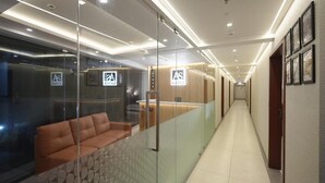 A hotel corridor with glass partitions, a reception desk, and a sofa. - AS Suites (Kanayannur)