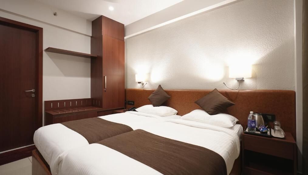 A hotel room with a large bed, two bedside tables, a wardrobe, and wall-mounted lights.